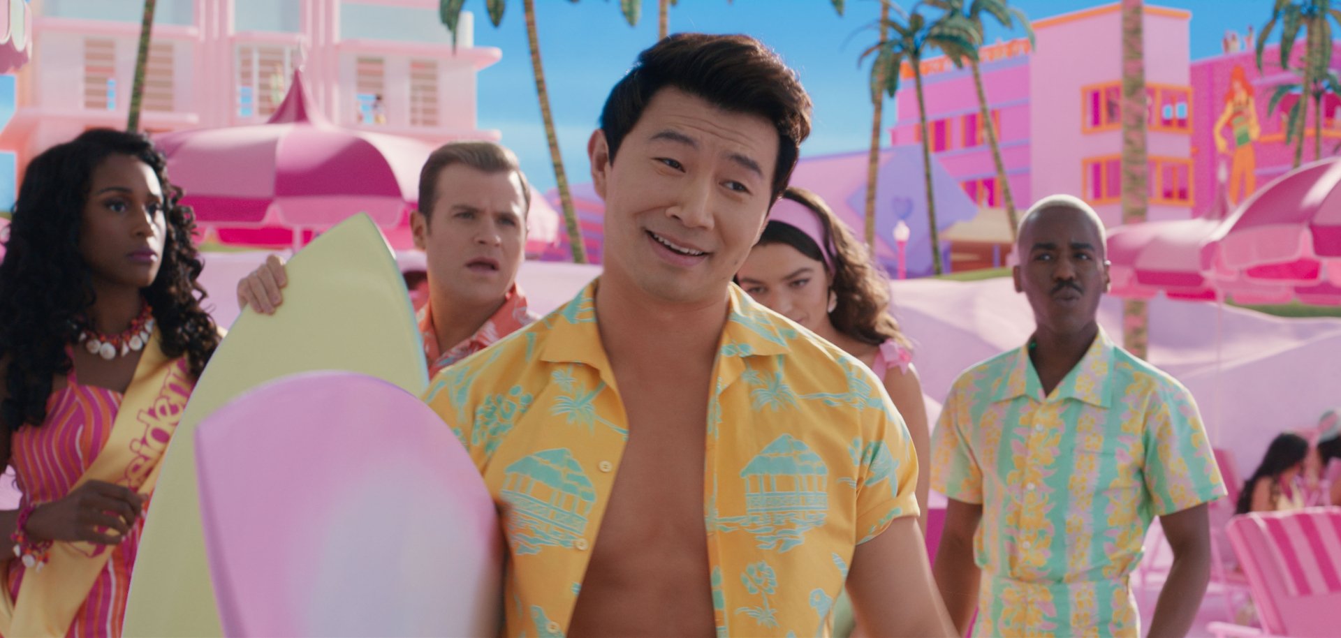 HD desktop wallpaper featuring a scene from the 2023 Barbie movie with Simu Liu wearing a vibrant yellow shirt, surrounded by cheerful characters in a colorful, whimsical setting.