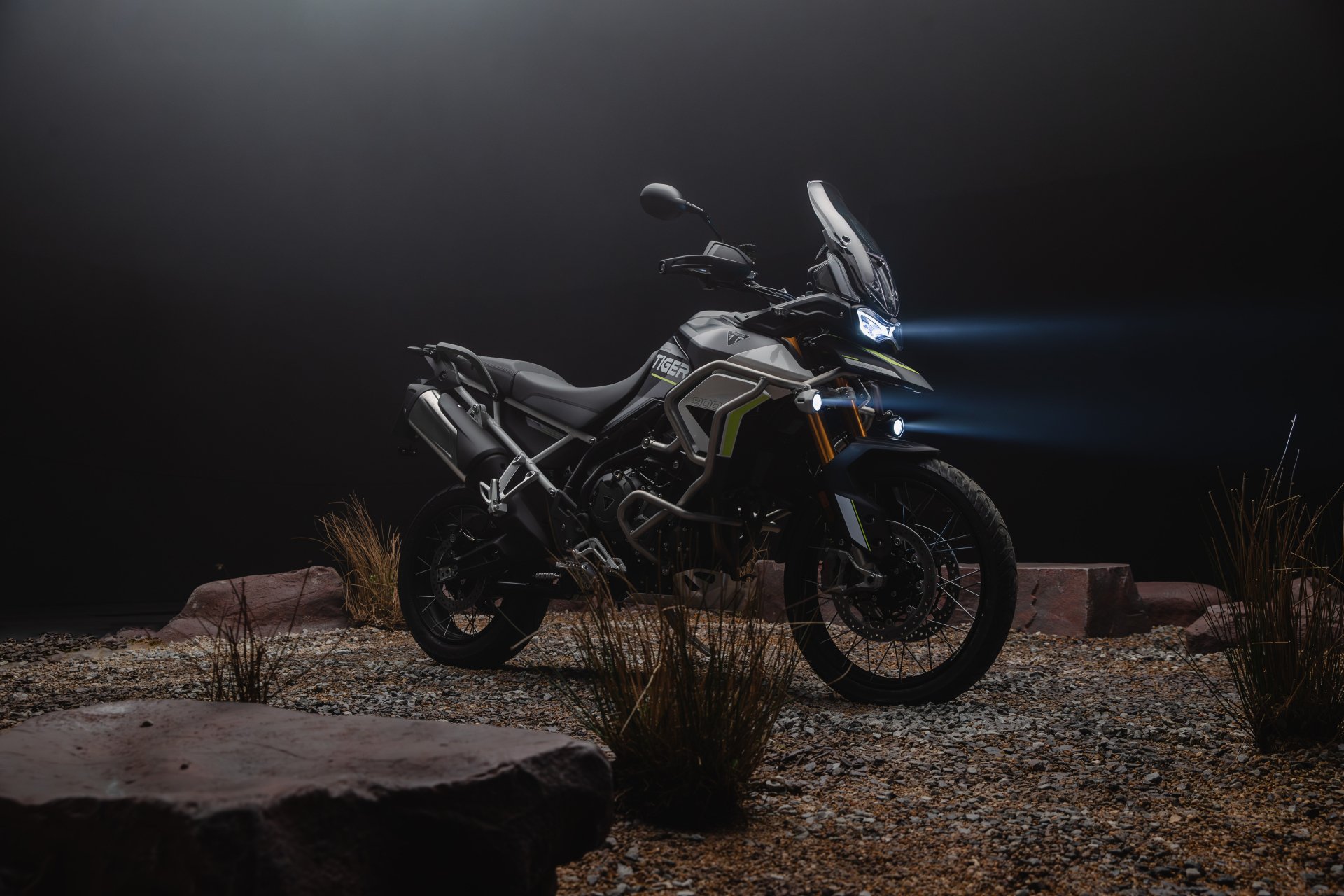 Triumph Tiger 900 Rally motorcycle parked outdoor at night with headlights on, HD desktop wallpaper.