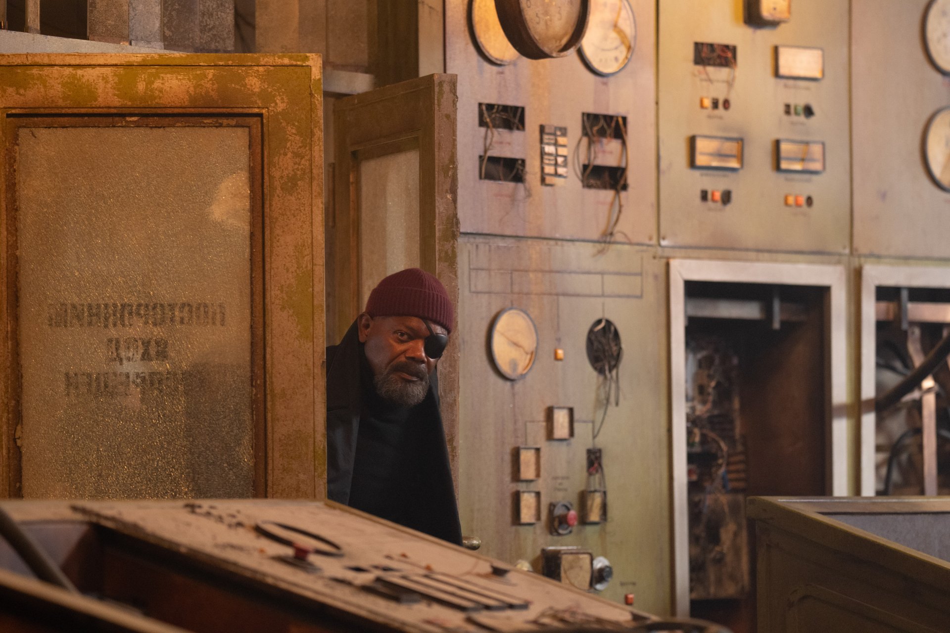 HD desktop wallpaper featuring a character reminiscent of Nick Fury in Secret Invasion themed setting, looking intently from behind industrial equipment.