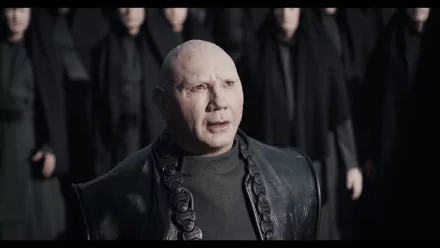 HD wallpaper featuring a character from Dune: Part Two, portrayed by an actor, standing with a solemn expression in front of a group of figures in dark attire.