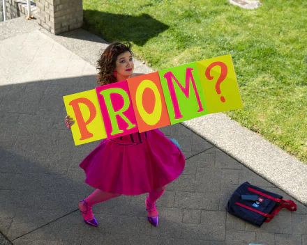 Young woman in a vibrant pink dress holding a colorful sign asking PROM? — Prom Pact theme HD desktop wallpaper and background.