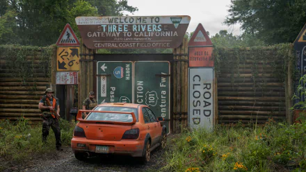 HD wallpaper of a scene from Twisted Metal showing an abandoned orange car in a rundown environment with signs indicating Three Rivers, set as a gloomy and atmospheric desktop background.
