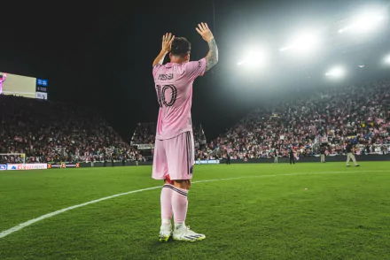 HD desktop wallpaper featuring Lionel Messi in a pink Inter Miami CF kit, applauding on the pitch in front of a packed stadium at night.