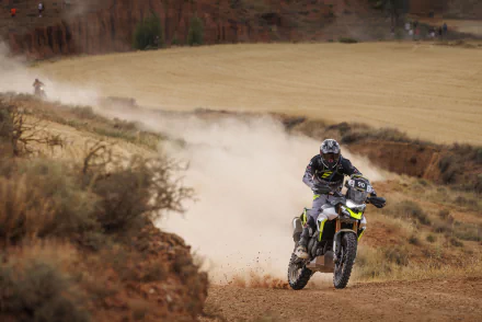 HD wallpaper of a Triumph Tiger 900 Rally Pro motorcycle riding off-road, kicking up dust on a rugged trail.