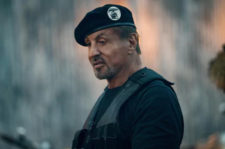 HD desktop wallpaper featuring a focused individual in a beret and tactical vest, with a blurry background, tagged as Expend4bles and inspired by Sylvester Stallone's iconic style.