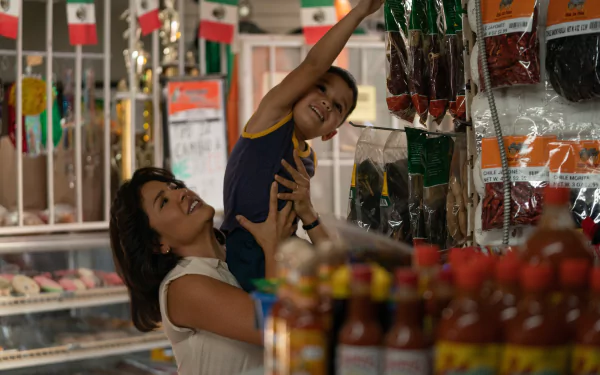 HD wallpaper of a heartwarming moment with a smiling woman lifting a young boy in a grocery store aisle, with shelves full of spicy Flamin' Hot snacks in the background.