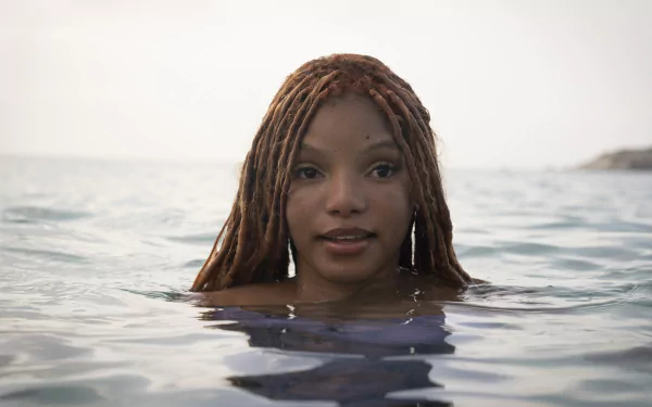 A serene HD background from the movie The Little Mermaid (2023), featuring a character with long hair, partially submerged in tranquil waters, exuding a sense of wonder and beauty.