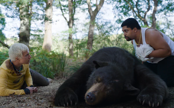 HD desktop wallpaper featuring two concerned people crouching beside a tranquilized bear in a forest setting, tagged as Cocaine Bear.