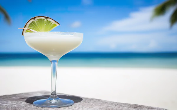 HD desktop wallpaper featuring a refreshing Daiquiri garnished with a lime slice, set against a vibrant beach backdrop.