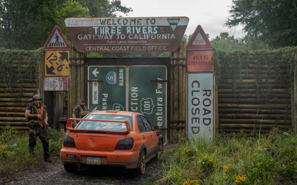 HD wallpaper of a scene from Twisted Metal showing an abandoned orange car in a rundown environment with signs indicating Three Rivers, set as a gloomy and atmospheric desktop background.