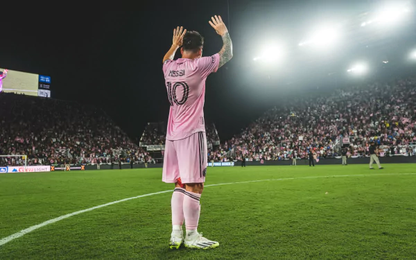 HD desktop wallpaper featuring Lionel Messi in a pink Inter Miami CF kit, applauding on the pitch in front of a packed stadium at night.