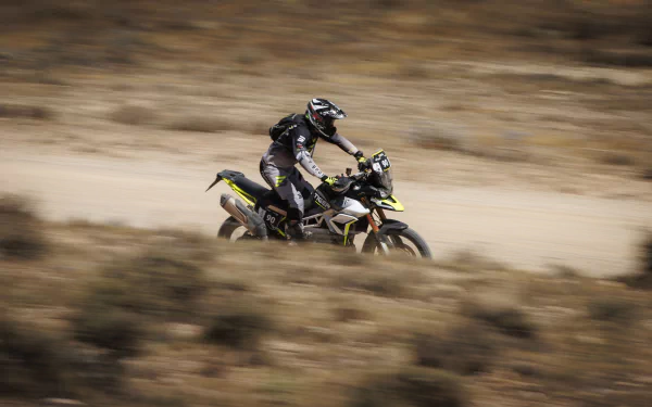 Motorcyclist riding a Triumph Tiger 900 Rally Pro across a rugged landscape, captured in motion as an HD desktop wallpaper and background.