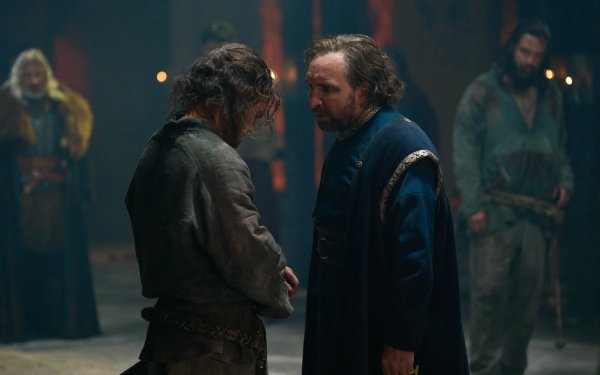 HD wallpaper featuring a scene with two characters from 'The Winter King', one, possibly Eddie Marsan, in a blue cloak engaging with another in a grim, medieval setting.