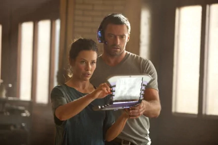 HD PC desktop wallpaper featuring Evangeline Lilly and Hugh Jackman in a scene from the movie Real Steel, focused on a digital device in a warmly lit room.
