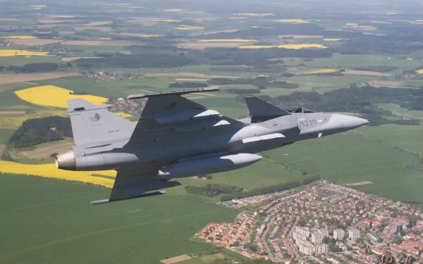 HD desktop wallpaper featuring a Saab JAS 39 Gripen jet fighter soaring over patchwork fields and a town, showcasing military aviation in flight.