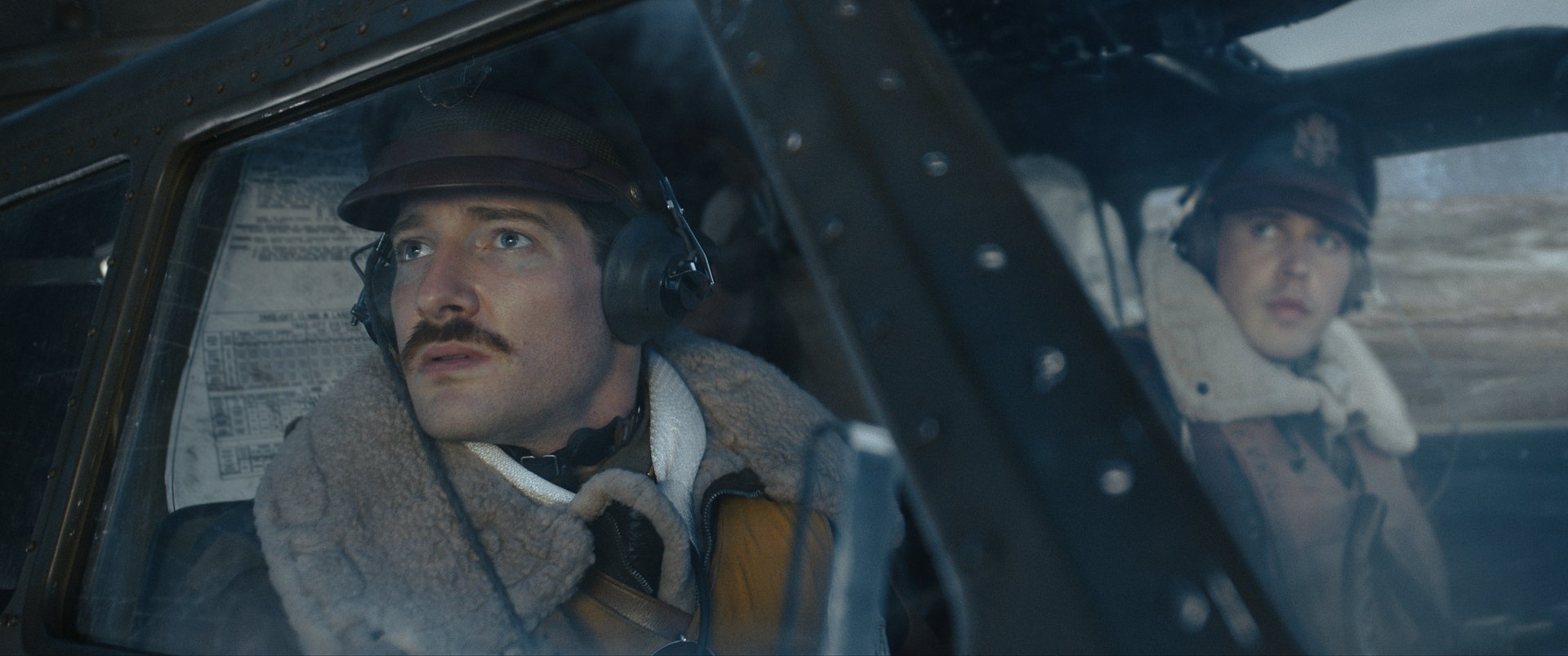 Two actors portraying World War II airmen in the cockpit of a bomber from the TV show Masters of the Air, in a high-definition desktop wallpaper.