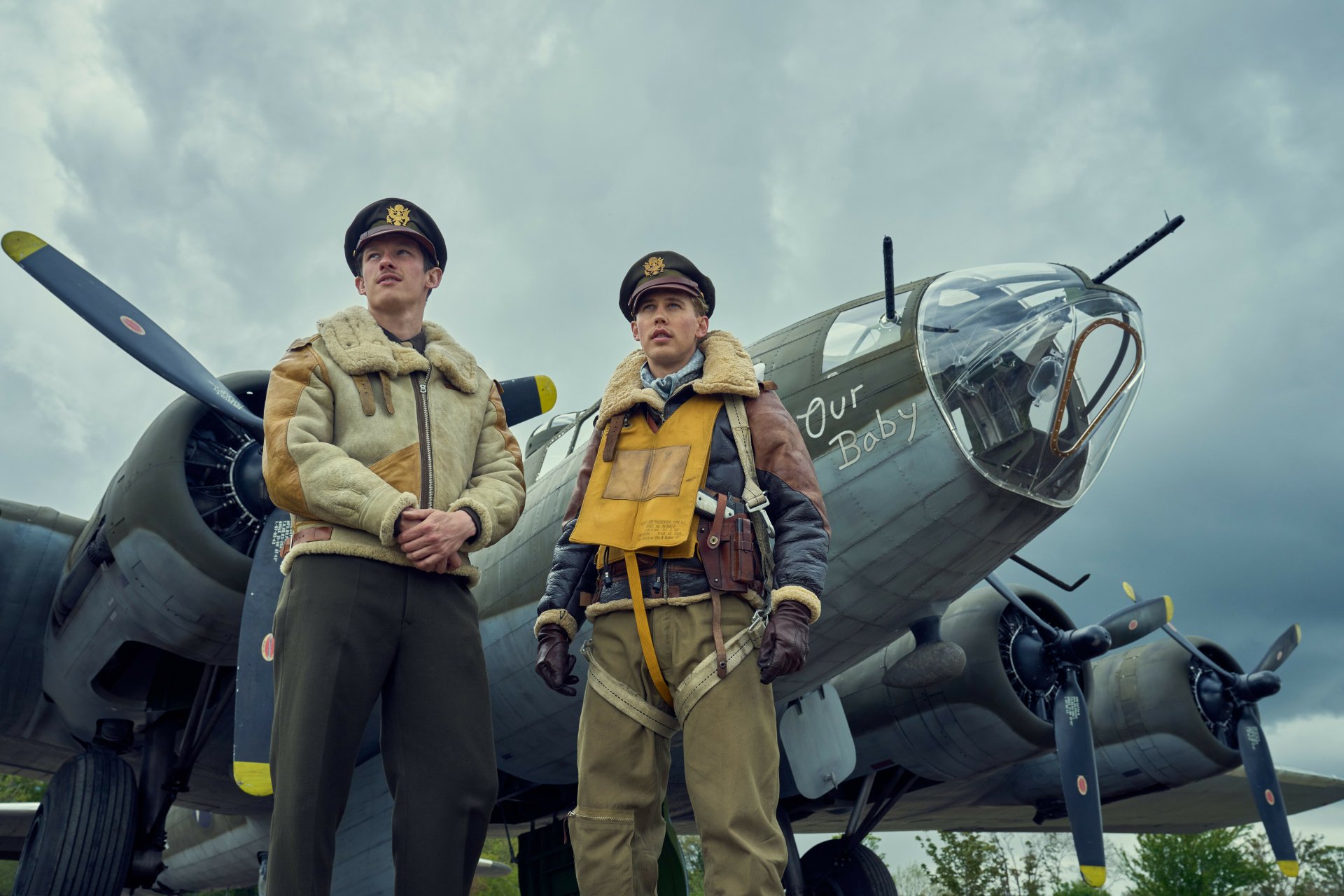 HD wallpaper featuring two actors from the TV show 'Masters of the Air' standing confidently in front of a vintage military aircraft, capturing the drama of World War II aviation.