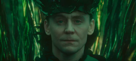 A striking HD wallpaper featuring Loki from Marvel Comics, portrayed by Tom Hiddleston, with an intense gaze against a backdrop of vibrant green foliage.