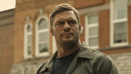 HD wallpaper featuring an intense male actor from the TV show Reacher, set against an urban backdrop.