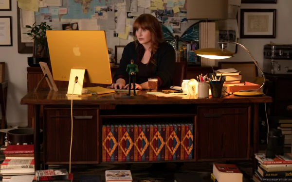 HD desktop wallpaper featuring a scene from Argylle movie with a character at a wooden desk with a laptop and office supplies.