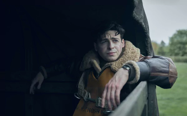 Actor in character dressed as a World War II airman from the TV show 'Masters of the Air,' peering out from an aircraft, ready to be used as a high-definition desktop wallpaper or background.