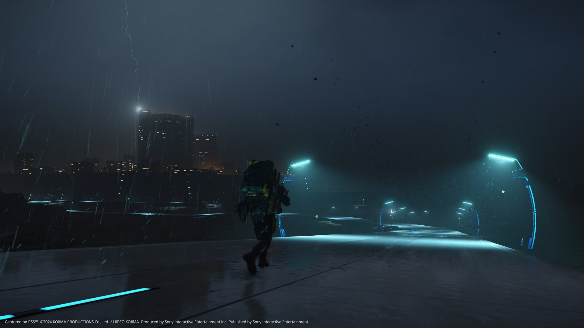 HD wallpaper of a mysterious figure in Death Stranding 2: On The Beach video game with futuristic cityscape background.