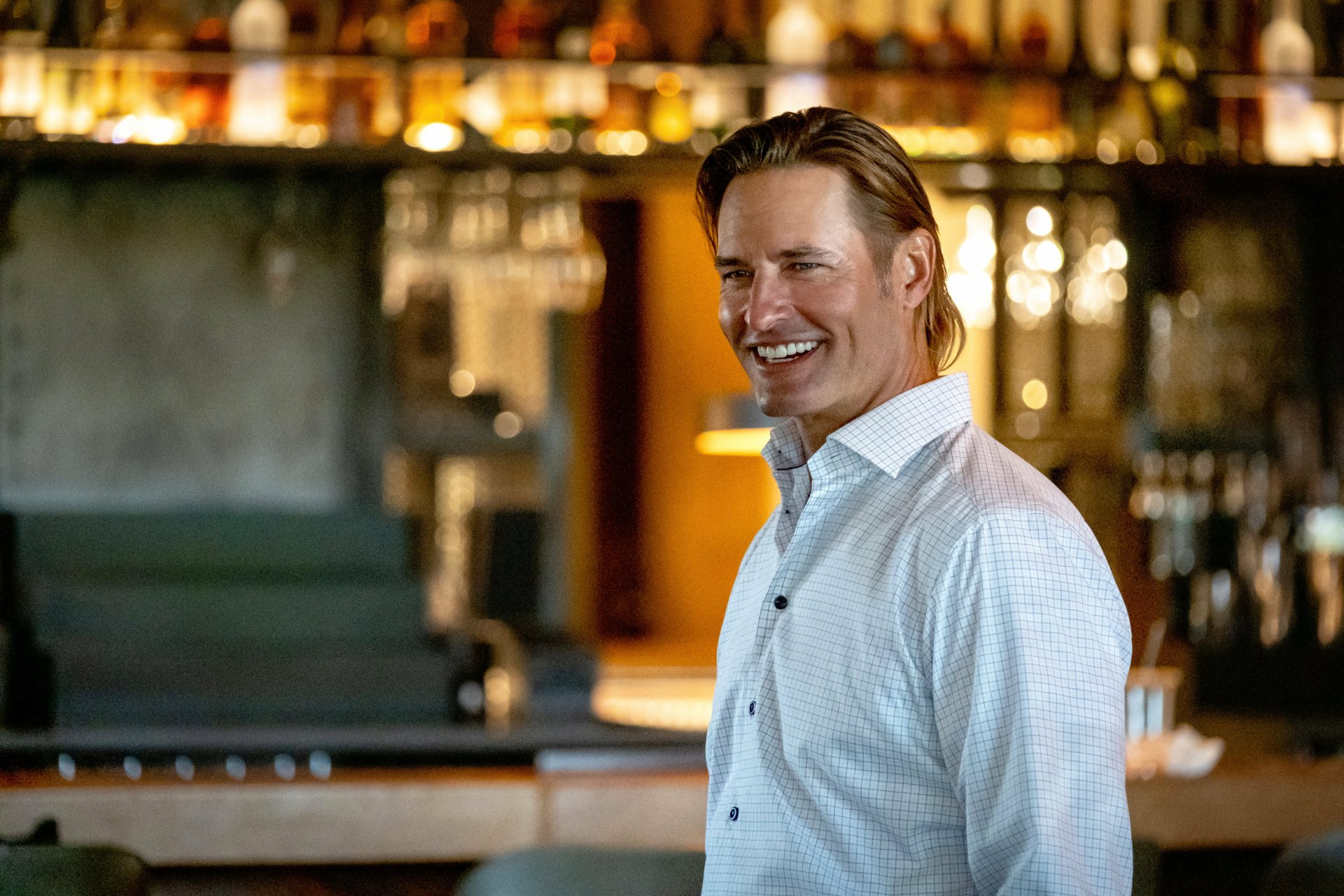 Smiling man from the TV show Yellowstone posing in a bar setting for a high-definition desktop wallpaper.