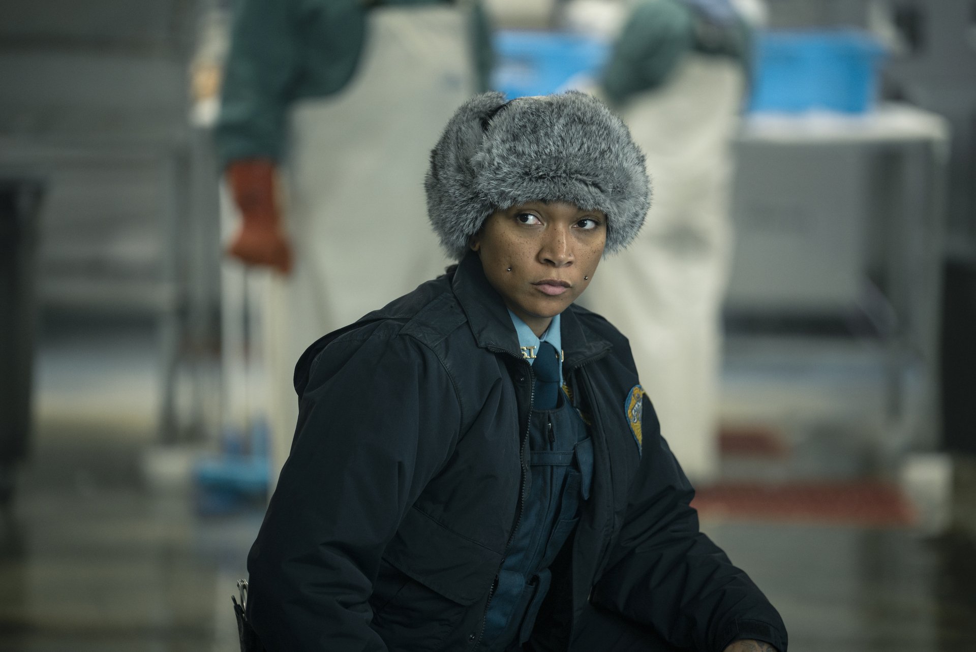 A scene from the TV show True Detective, featuring a focused character in a fur hat, set against a backdrop of a busy investigation scene. This high-definition image serves as a striking desktop wallpaper.