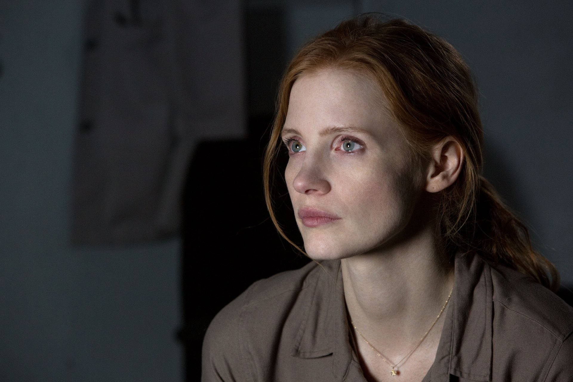 HD wallpaper featuring an introspective moment from the movie Interstellar with a female character showing a thoughtful expression in a dimly lit room.