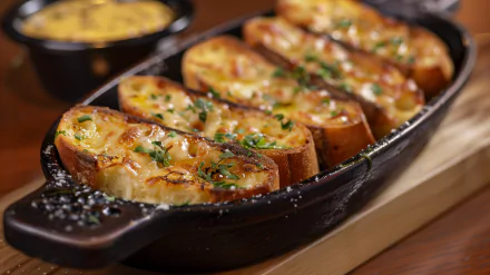 Delicious garlic bread sliced and baked to perfection, garnished with herbs, served in a cast iron dish. A mouthwatering food scene for an HD desktop wallpaper.