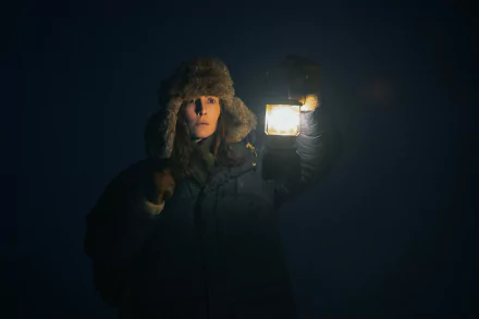 HD wallpaper featuring a mysterious scene from the TV show Constellation (2024) with a character in winter attire holding a lantern in the dark.