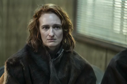 A close-up of a character from the TV show The Walking Dead: The Ones Who Live, featuring a woman with curly red hair, wearing a dark fur coat, set against a muted background.