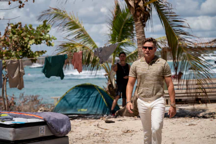 HD desktop wallpaper featuring a scene from the movie Road House (2024) with a focus on actor Billy Magnussen walking on a beach with palm trees and camping gear in the background.