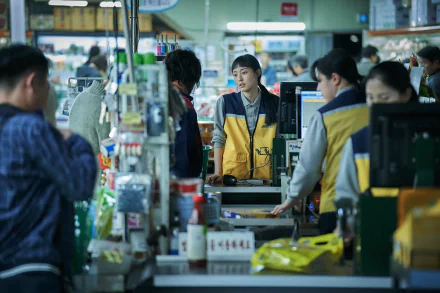 A HD wallpaper capturing a scene from the TV show Parasyte: The Grey with individuals inside a grocery store, highlighting a cashier in a yellow vest.