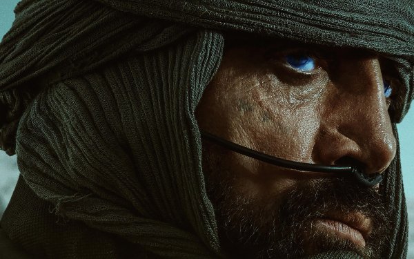 Close-up HD wallpaper featuring a character from the movie Dune (2021) with distinctive blue eyes, wrapped in a desert headscarf, intense and contemplative.