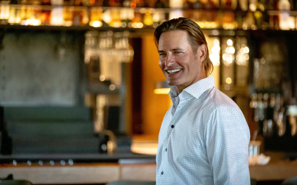 Smiling man from the TV show Yellowstone posing in a bar setting for a high-definition desktop wallpaper.