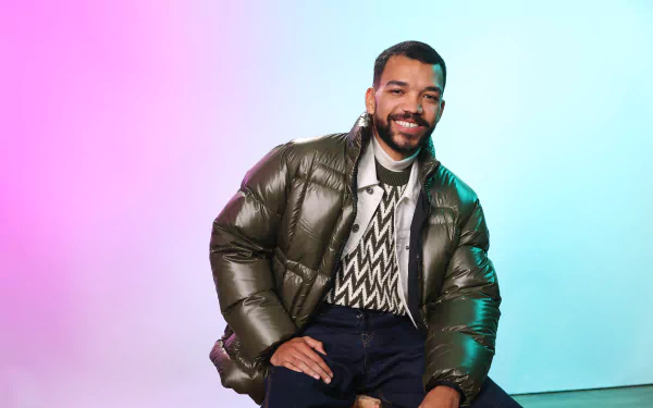 Actor from The American Society of Magical Negroes TV show in a stylish outfit against a vibrant pink and blue gradient background for HD desktop wallpaper.