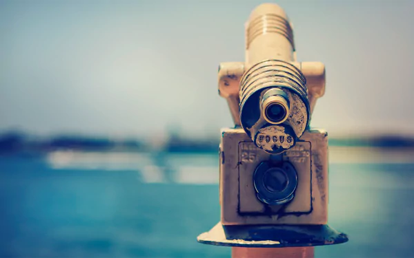 A close-up of a man-made telescope overlooking a serene body of water, set against a vibrant blue sky, creating a captivating HD desktop wallpaper.