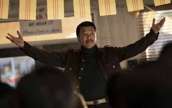 Man standing with arms outstretched in front of a crowd in a scene from the TV show The Sympathizer, used as an HD desktop wallpaper and background.