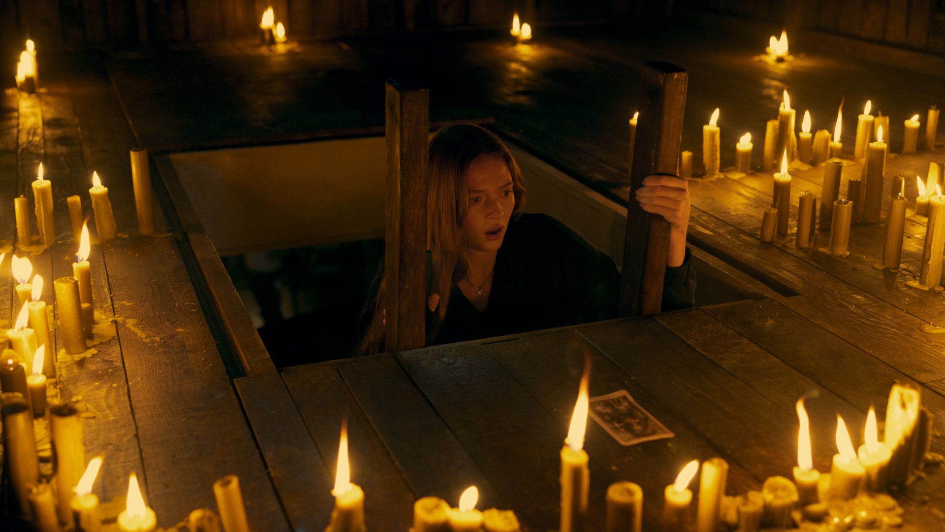 HD desktop wallpaper from Tarot (2024) featuring a scene with a woman surrounded by candles in a mysterious, dimly lit wooden setting.