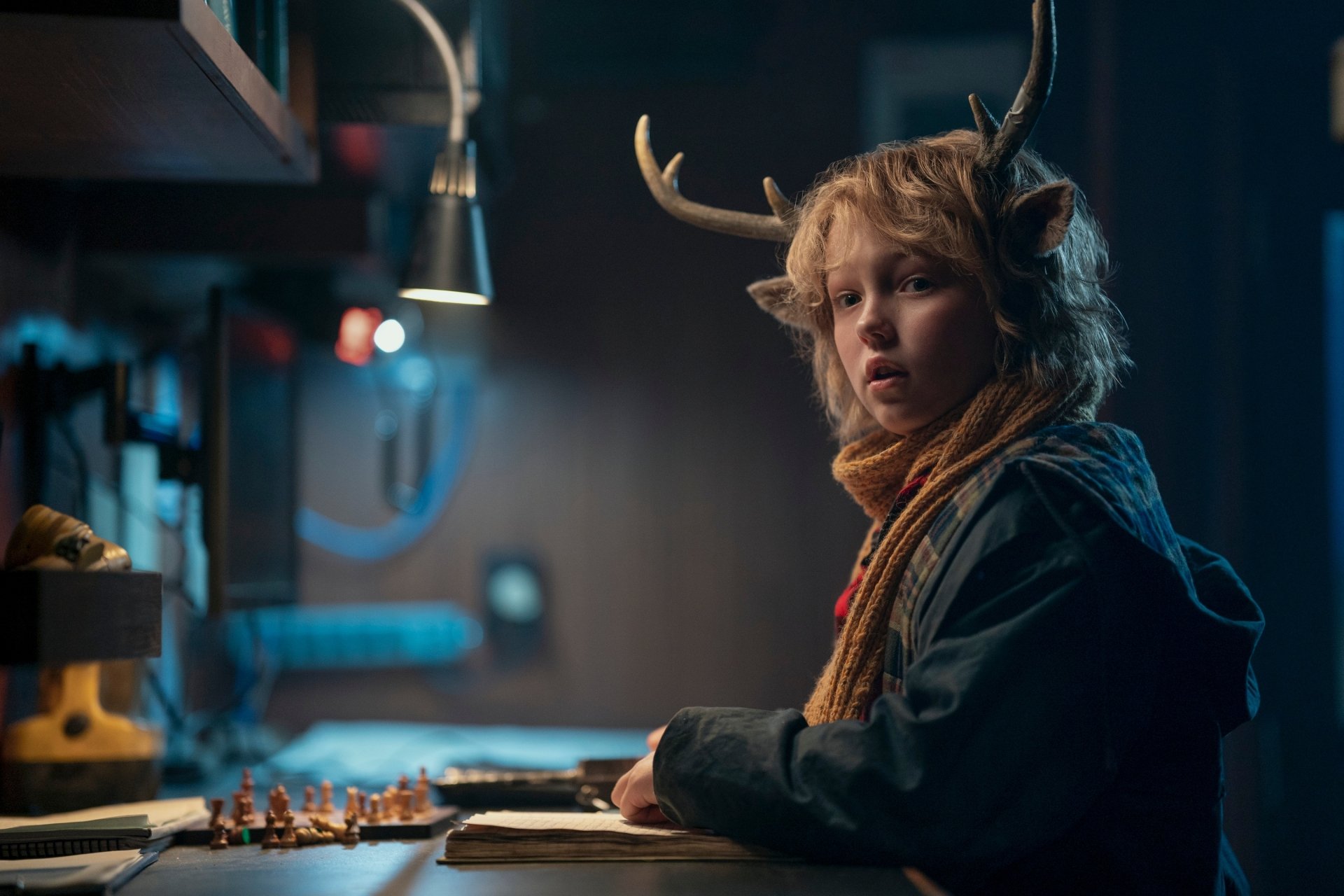 HD wallpaper of Gus (Sweet Tooth), portrayed by Christian Convery in the TV show Sweet Tooth, features a boy with antlers sitting at a desk in a dimly lit room.