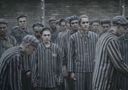 HD desktop wallpaper from the TV show The Tattooist of Auschwitz, featuring a somber scene of prisoners in striped uniforms.