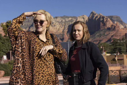 Two women stand outdoors against a backdrop of mountains, showcasing a scene from the TV show Hacks (2021). One woman wears a leopard-print coat, while the other sports a casual look.