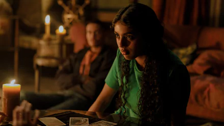 HD wallpaper from the movie Tarot (2024) featuring a woman reading tarot cards by candlelight with a man in the background.