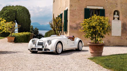 HD desktop wallpaper featuring a Morgan Midsummer parked in a picturesque courtyard with lush greenery and a scenic lake in the background.