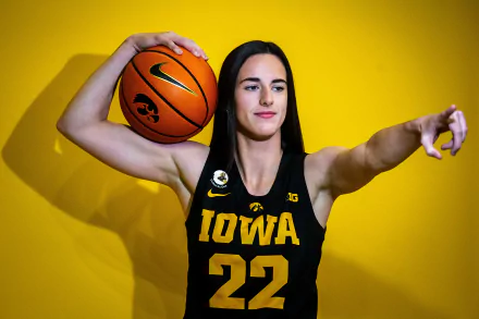 HD wallpaper of Caitlin Clark, a basketball player in Iowa uniform number 22, posing confidently against a yellow background, with a basketball in one hand and pointing with the other.