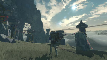 A high-definition desktop wallpaper featuring a video game scene with a character standing near a cairn set against a mountainous backdrop under a partly cloudy sky.