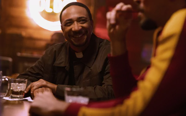 A still from the TV show 'The Big Door Prize' featuring two characters enjoying a conversation in a bar with a warm, cozy atmosphere, suitable as an HD desktop wallpaper or background.