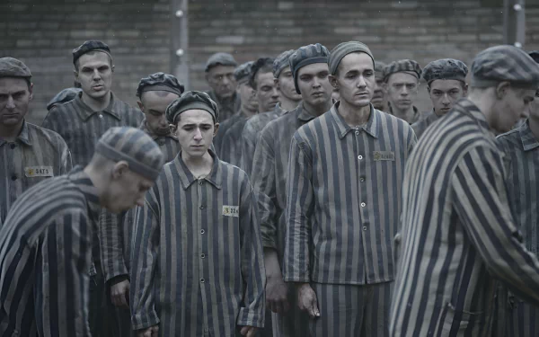 HD desktop wallpaper from the TV show The Tattooist of Auschwitz, featuring a somber scene of prisoners in striped uniforms.