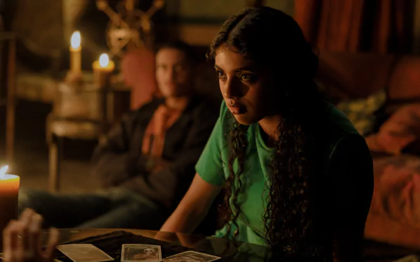 HD wallpaper from the movie Tarot (2024) featuring a woman reading tarot cards by candlelight with a man in the background.